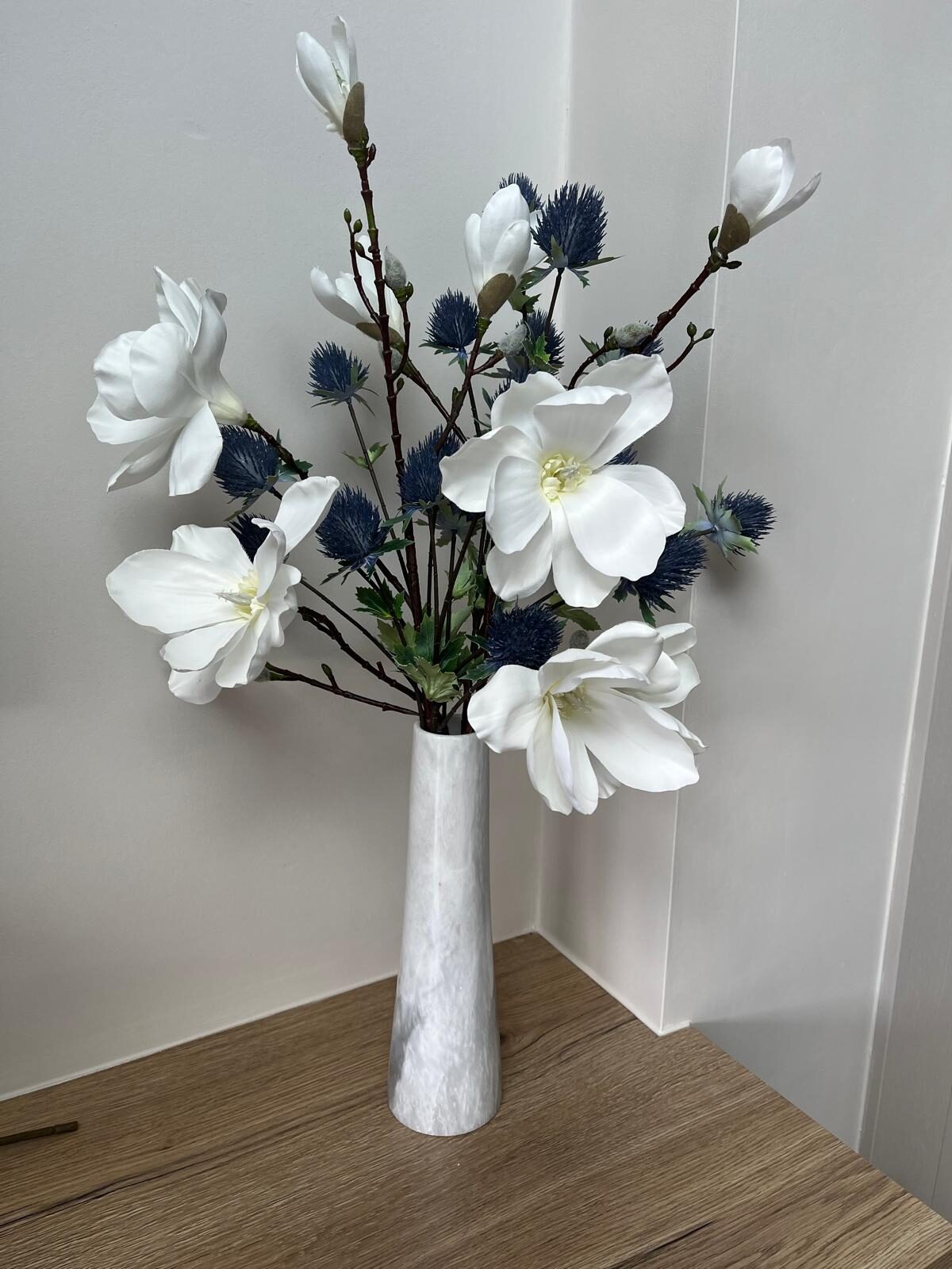 White magnolia and deep blue thistle faux arrangement in a pale marble vase