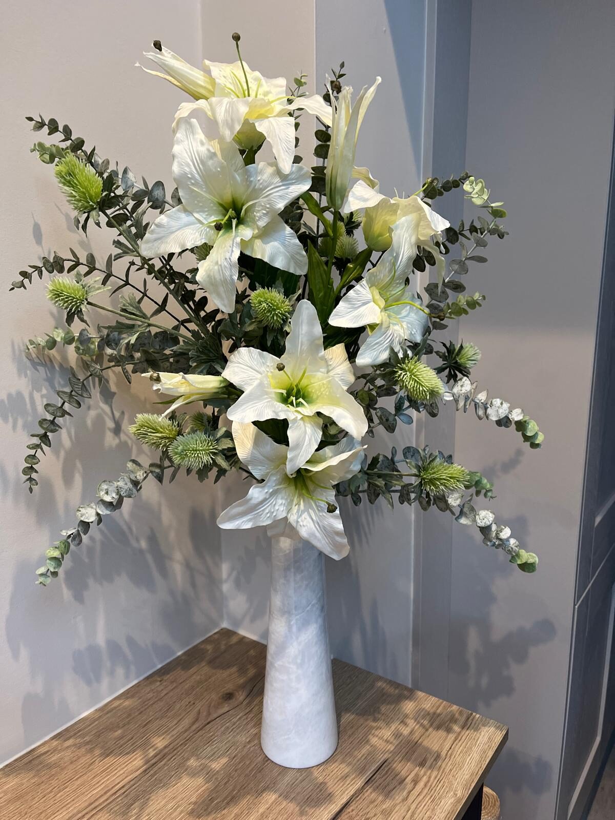 Silk lilies, eucalyptus and pale green thistle faux arrangement in a pale grey marble vase, approx 80cm