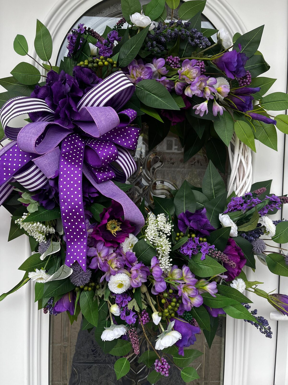 Purple spring faux wreath with lavender and polka-dot ribbons on a white willow base