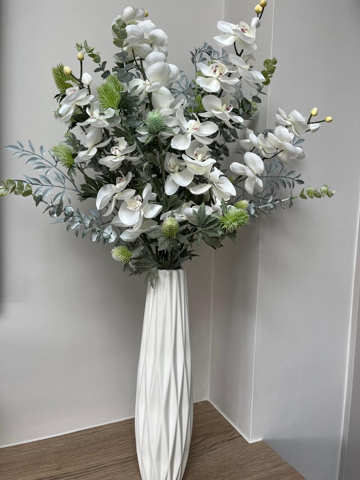 White silk orchid faux arrangement with pale green thistle, palest grey eucalyptus and fern in a white vase